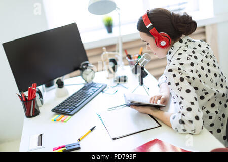 Schönes junges Mädchen sitzt in Kopfhörern und mit einem Notizblock am Tisch im Büro und spricht in das Mikrofon. Stockfoto