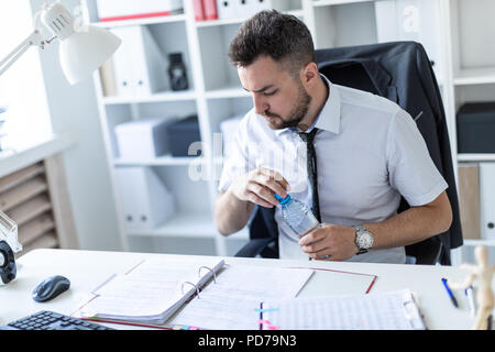 Ein Mann sitzt an einem Tisch im Büro, Arbeiten mit Dokumenten und öffnen eine Flasche Wasser. Stockfoto