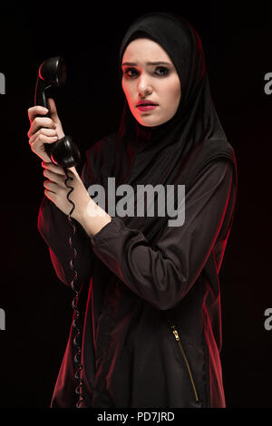 Porträt der schönen schweren Angst junge muslimische Frau mit schwarzen Hijab um Hilfe ruft auf schwarzem Hintergrund Stockfoto
