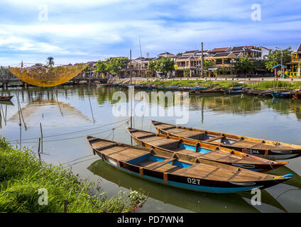 Drei kleine Ruderboote aufgereiht im Fluss mit Geschäften über den Fluss und ein Netz über dem Fluss. Stockfoto