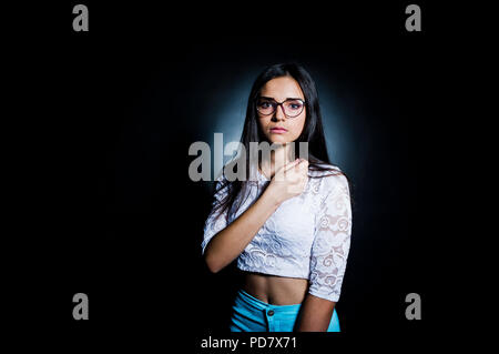 Portrait einer attraktiven jungen Frau in weißen und blauen Hosen mit ihrer Brille in die dunklen Stellen. Stockfoto