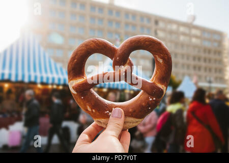 Ein Mädchen oder eine junge Frau hält einen traditionellen deutschen Brezel in der Straße. Oktoberfest im Hintergrund. Stockfoto