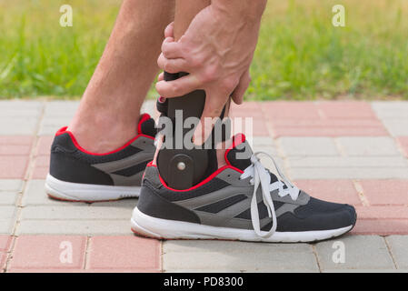 Mann in sportliche Turnschuhe tragen Sprunggelenk Orthese oder Bandage Stockfoto