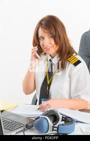 Schöne Frau pilot tragen Uniform mit Schulterklappen mit Handy und Laptop im Preflight Briefing Stockfoto