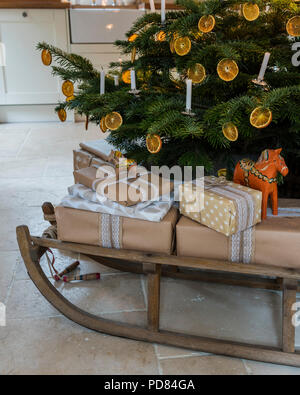 Eingepackten Geschenke auf einem hölzernen Schlitten unter Kerzenlicht beleuchteten Weihnachtsbaum Stockfoto