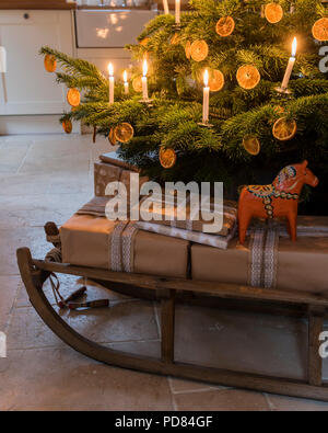 Eingepackten Geschenke auf einem hölzernen Schlitten unter Kerzenlicht beleuchteten Weihnachtsbaum Stockfoto