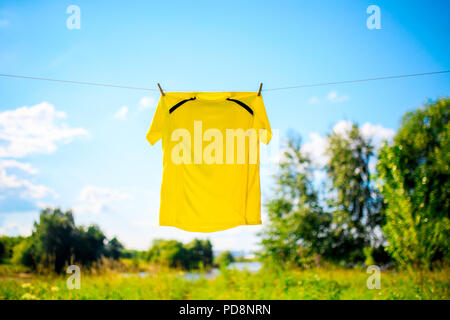 Foto von gelben T-Shirt hängen am Seil gegen den blauen Himmel mit Wolken Stockfoto