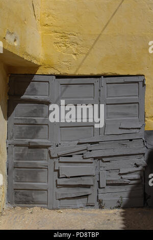 Gebäude mit gelber Fassade und grau Garage Tor, das gebrochen wurde und seine in nicht allzu detaillierte Weise repariert. El Jadida, Marokko. Stockfoto
