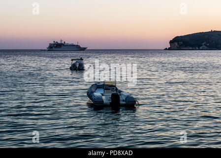 Aufblasbare Motorboote mit dem Kreuzfahrtschiff in der Ferne verankert am Ionischen Meer in der Nähe von Parga, Griechenland an der Blauen Stunde, Sonnenuntergang Stockfoto