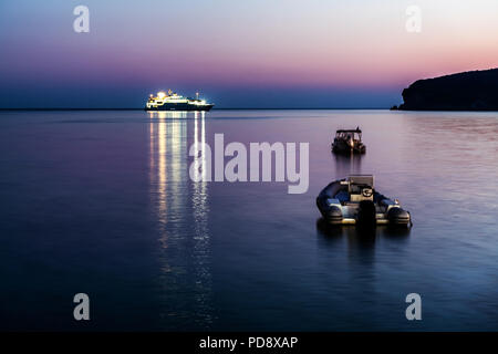 Aufblasbare Motorboote mit dem Kreuzfahrtschiff in der Ferne verankert am Ionischen Meer in der Nähe von Parga, Griechenland an der Blauen Stunde, Sonnenuntergang Stockfoto