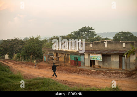 Geschäfte und Häuser säumen den Straßenrand von einer kleinen Stadt im ländlichen Bezirk Mukono, Uganda. Stockfoto