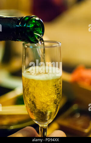 Gießen Champagner aus einer Flasche in ein Glas Wein in der Hand auf einem unscharfen Hintergrund Stockfoto