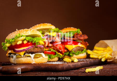 Drei verschiedene leckere Burger mit Rindfleisch, Tomaten, Käse, Gurken, Zwiebeln und Salat auf Holztisch und braunen Hintergrund mit Kopie Raum Stockfoto