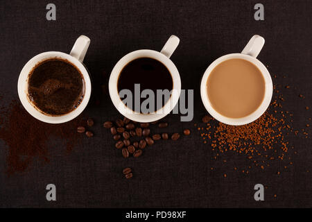 Drei Tassen Kaffee mit Boden, Instant Kaffee und gerösteten Bohnen auf dunklem Hintergrund von oben. Stockfoto
