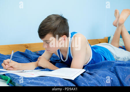 Kaukasische Teenager Festlegung auf seinem Bett Hausaufgaben Stockfoto