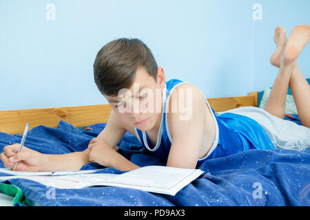 Kaukasische Teenager auf dem Bett und liest ein Lehrbuch. Stockfoto