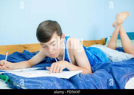 Kaukasische Teenager auf dem Bett und liest ein Lehrbuch. Stockfoto