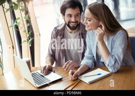Junge Leute Mann und Frau gemeinsam Coworking an den kreativen stilvolle Büro am Tisch sitzen, Musik hören auf Laptop lächelnd, fröhlich zu pop Stockfoto