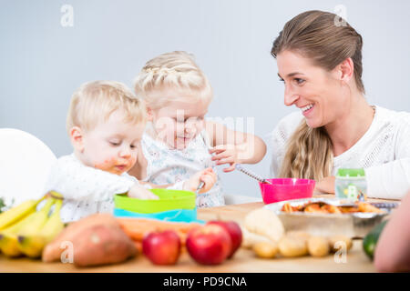 Portrait von eine glückliche Mutter von zwei Kindern am Tisch sitzen Stockfoto