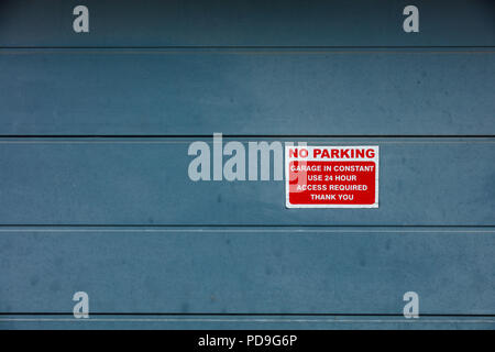 Kleines deutliches rot-weißes Schild ohne Parken an der modernen blauen Garagentür. Frontale flache Komposition mit klarem Signal für den städtischen Wohnbereich mit Kopierraum. Stockfoto