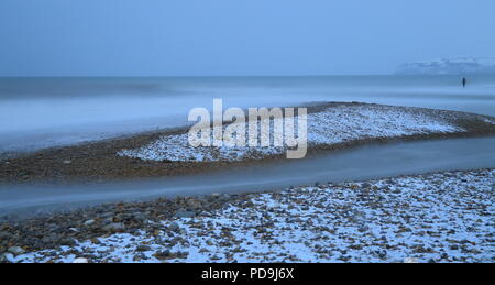 Verschwommen meer wellen auf einem Kieselstrand im Schnee in der Nähe der Stadt von Seaton in Devon abgedeckt Stockfoto