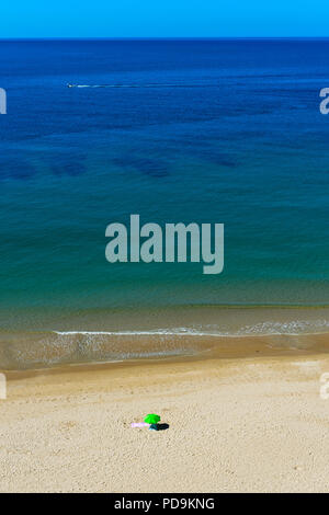 Einsamer Sonnenschirm auf einer leeren Sandstrand in der Nähe von Praia da Luz, Algarve, Portugal Stockfoto