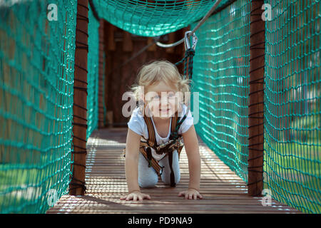Kleine blonde Mädchen überwindet ein Hindernis im Seilpark. Sie kriechen Stockfoto