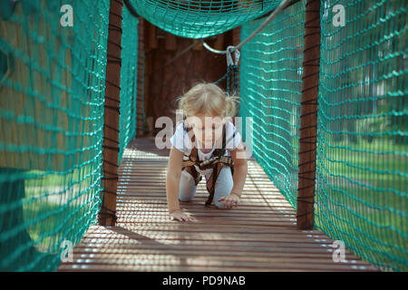 Kleines Mädchen überwindet ein Hindernis im Seilpark. Sie kriechen. Stockfoto