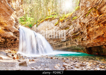 Morgensonne späht durch den Wald wie ein Wasserfall in der Johnston Canyon Creek im Banff National Park in Alberta, Kanada fließt. Johnston Canyon ist ein p Stockfoto