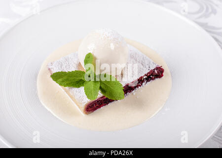 Berry Apfelstrudel Kuchen serviert mit Eis, minzblatt und Vanillesauce. Klassische österreichische Dessert auf weiße Platte. Süßes Dessert im Restaurant. Morgen Licht. Stockfoto