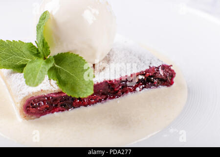 Berry Apfelstrudel Kuchen serviert mit Eis, minzblatt und Vanillesauce. Klassische österreichische Dessert auf weiße Platte. Süßes Dessert im Restaurant. Morgen Licht. Stockfoto