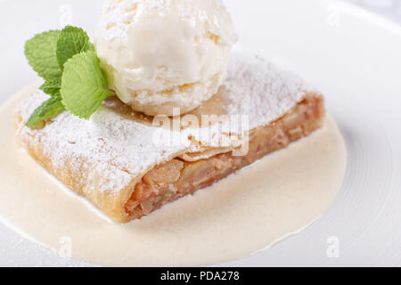 Obst Apfelstrudel Kuchen serviert mit Eis, minzblatt und Vanillesauce. Klassische österreichische Dessert auf weiße Platte. Süßes Dessert im Restaurant. Morgen Licht. Stockfoto