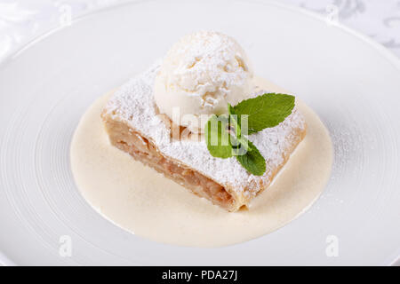 Obst Apfelstrudel Kuchen serviert mit Eis, minzblatt und Vanillesauce. Klassische österreichische Dessert auf weiße Platte. Süßes Dessert im Restaurant. Morgen Licht. Stockfoto