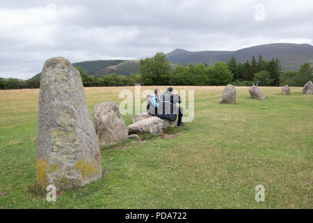 Ein paar setzte sich auf einen Stein auf Castlerigg Steinkreis einen Snack mit großen Stein an der Front und im Lake District Berge im Hintergrund Stockfoto