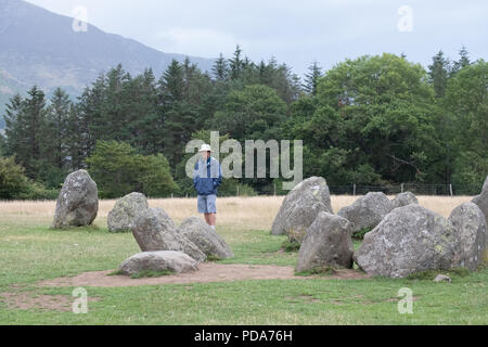 Single Gentleman mit unter die Steine von Castlerigg Steinkreis, Lake District, Cumbria, UK mit grünen Bäumen und Lakeland Hügel hinter. Stockfoto