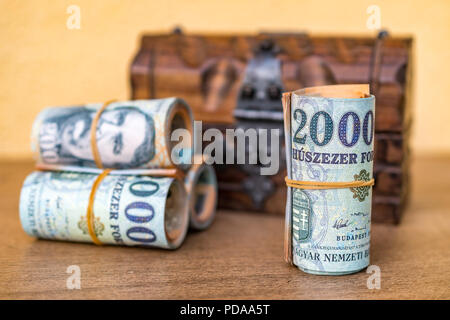 Aufgerollt und 20000 Forint Banknoten gestapelt mit einem geschlossenen vintage Holzkiste im Hintergrund Stockfoto