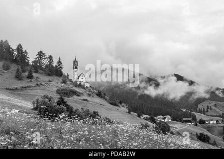 Kirche in Schwarz und Weiß an einem nebligen Hang in die Dolomiten in La Valle, Südtirol, Italien Stockfoto