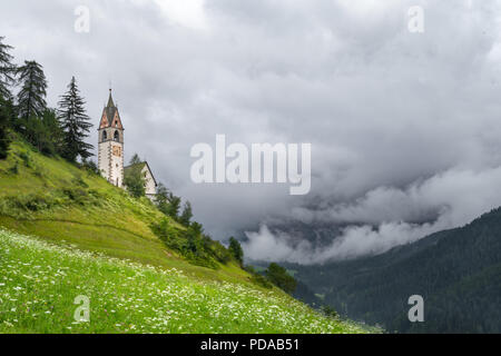 Kirche auf einem nebligen Hang, Wolken wirbelnden in einem Tal in den Dolomiten in La Valle, Südtirol, Italien Stockfoto