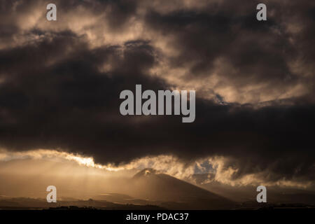 Sonnenlicht am frühen Morgen durch dunkle Gewitterwolken über dem Berg von Tejina in Guia de Isora im Westen von Teneriffa, Kanarische Inseln, Spanien Stockfoto