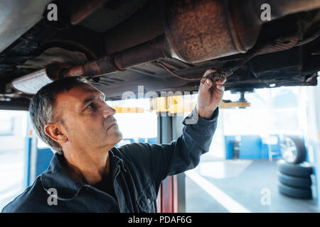 Reparatur Mann Prüfen der Kabel unter dem Auto im Service Station. Mechanische Prüfung der elektrischen Verbindungen eines Automobils in seiner Garage. Stockfoto