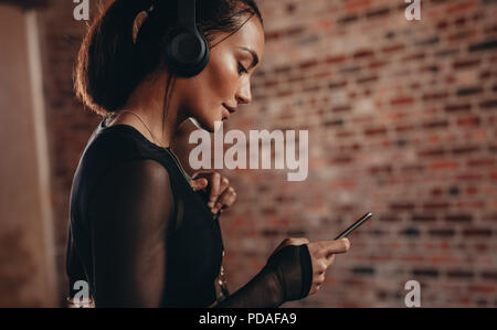 Nahaufnahme von passen junge Frau mit Kopfhörern hören von Musik von Ihrem Smartphone. Weibliche fitness Modell in der Turnhalle mit Handy. Stockfoto