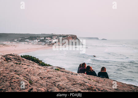 Eine Gruppe von Freundinnen Standortwahl auf einer Klippe mit einem selfie mit der Ansicht von Monte Clerigo Strand in Portugal vor Ihnen Stockfoto