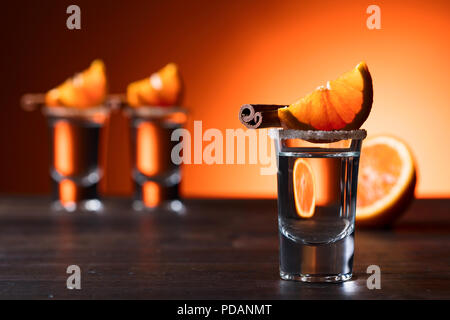Gläser tequila mit Orange und Zimt Sticks auf einen hölzernen Tisch. Stockfoto