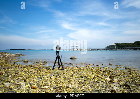 Kamera auf einem Stativ, Bild vom schönen Strand und weiße Brücke im blauen Himmel mit ND-Filter. Stockfoto