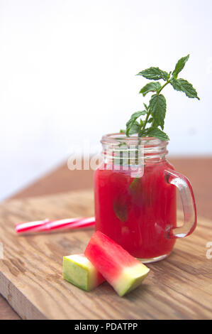 Glas Glas mit Wassermelone Saft mit einem Zweig von Grüner Minze und kleine Segmente der Wassermelone Stockfoto