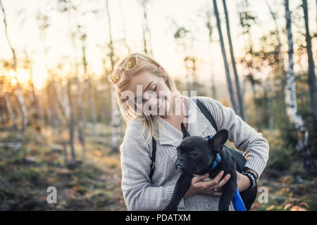 Junge blonde Frau mit ihrer französischen Bulldogge Welpe in sonniger Tag. Stockfoto