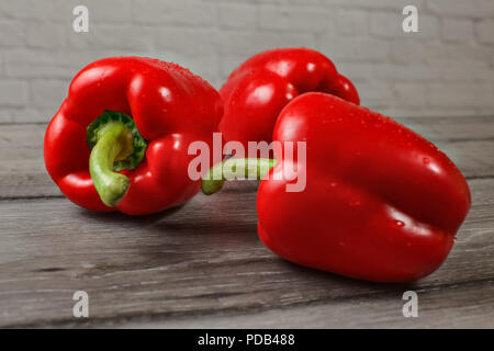 Drei helle rote Paprika auf hölzernen Schreibtisch, Fokus auf abfällt, Wasser. Stockfoto
