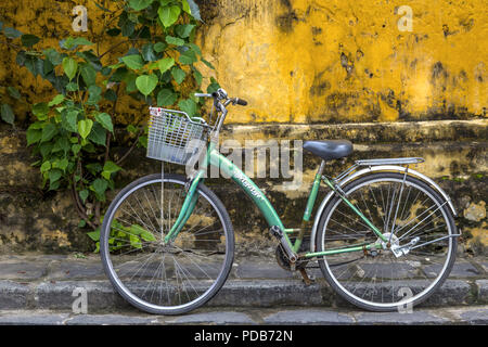 Ein grünes Fahrrad geparkt außerhalb entlang einer alten gelben Gebäude in der Altstadt von Hoi An. Stockfoto