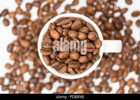 Weißes Porzellan Espresso Tasse gesehen von oben auf weißem Hintergrund mit braunen geröstete Kaffeebohnen überlaufen Stockfoto