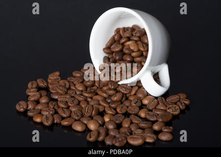 Geröstete Kaffeebohnen Verschütten von Weiß Espressotasse liegen auf der Seite und auf reflektierende Glas schwarz Oberfläche Stockfoto